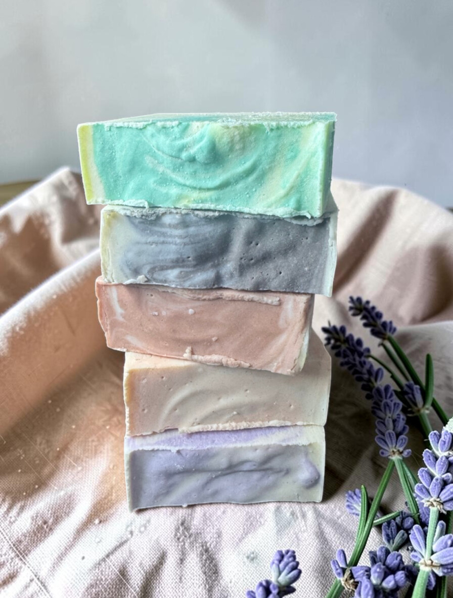 Tres jabones artesanales Serena en tonos lavanda, salvia y crema, sobre lino con ramas de lavanda y romero